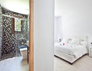 Une salle de bain moderne avec un mur recouvert de carreaux à motifs géométriques, une douche en verre et des toilettes blanches.