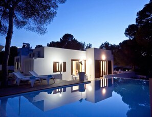 Une maison moderne dotée d’une piscine, de chaises longues et d’une entrée bien éclairée.