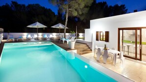 Un espace piscine extérieur moderne, doté de chaises longues et de parasols, d’un escalier menant à un niveau supérieur et d’une entrée avec porte vitrée.