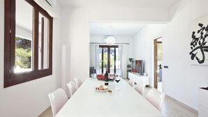 Un espace repas moderne avec une table blanche et des chaises à coussins rouges, une grande fenêtre et une vue sur l’extérieur.