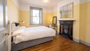 A bedroom with a bed, a window, a mirror, a fireplace, and a lamp.
