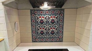 A kitchen with a black induction cooktop, a backsplash with floral tile design, and a white countertop.
