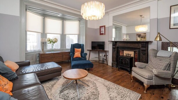 A living room with a fireplace, a blue armchair, a brown leather sofa, and a wooden coffee table.