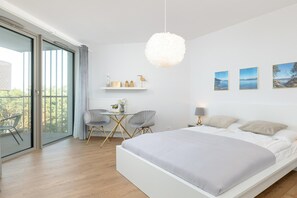 A modern bedroom with a large bed, a desk, two chairs, and a balcony with a view.