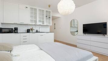Ein modernes Schlafzimmer mit einem Bett, einem Fernseher, einem Spiegel und einer Küchenzeile.