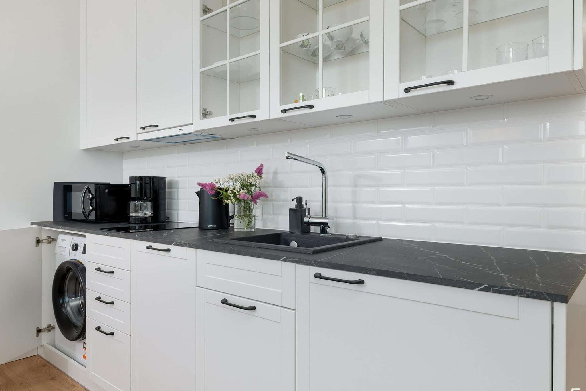 A modern kitchen with white cabinetry, a black countertop, a coffee maker, and a washing machine.