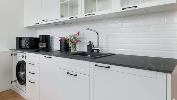 A modern kitchen with white cabinetry, a black countertop, a coffee maker, and a washing machine. - Beachfront holiday apartment, sauna, swimming pool (Pobierowo)