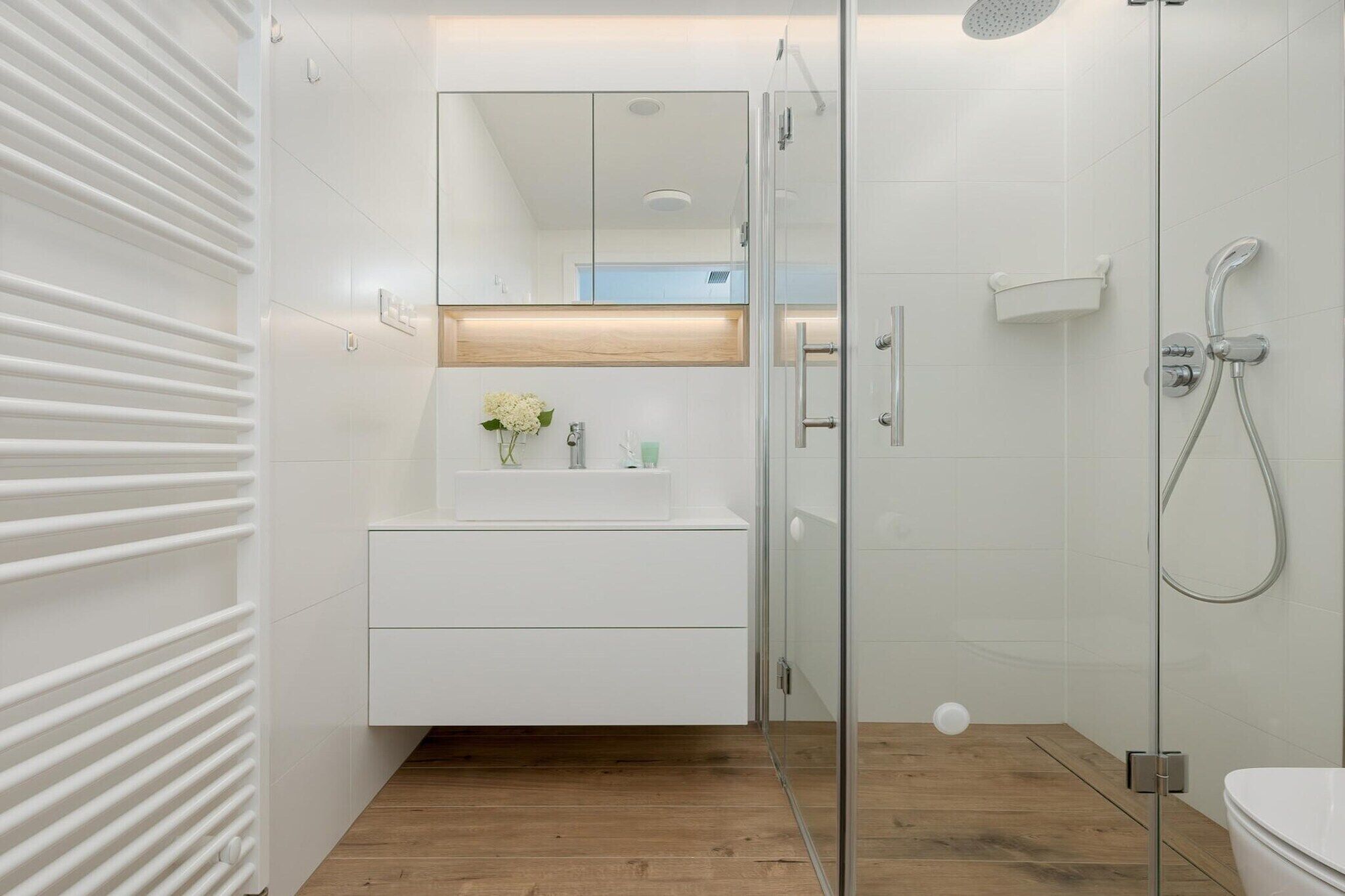 A modern bathroom with a glass shower enclosure, a white vanity with a mirror, and a wooden floor.
