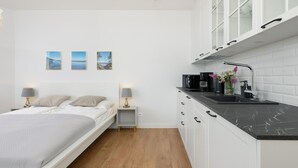 A modern bedroom with a bed, bedside lamps, and a nightstand. Adjacent is a kitchen with a black countertop, white cabinets, and a sink. - Beachfront holiday apartment, sauna, swimming pool (Pobierowo)