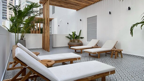 Una terrazza sul tetto con poltroncine in legno, piante in vaso e una struttura a pergola.