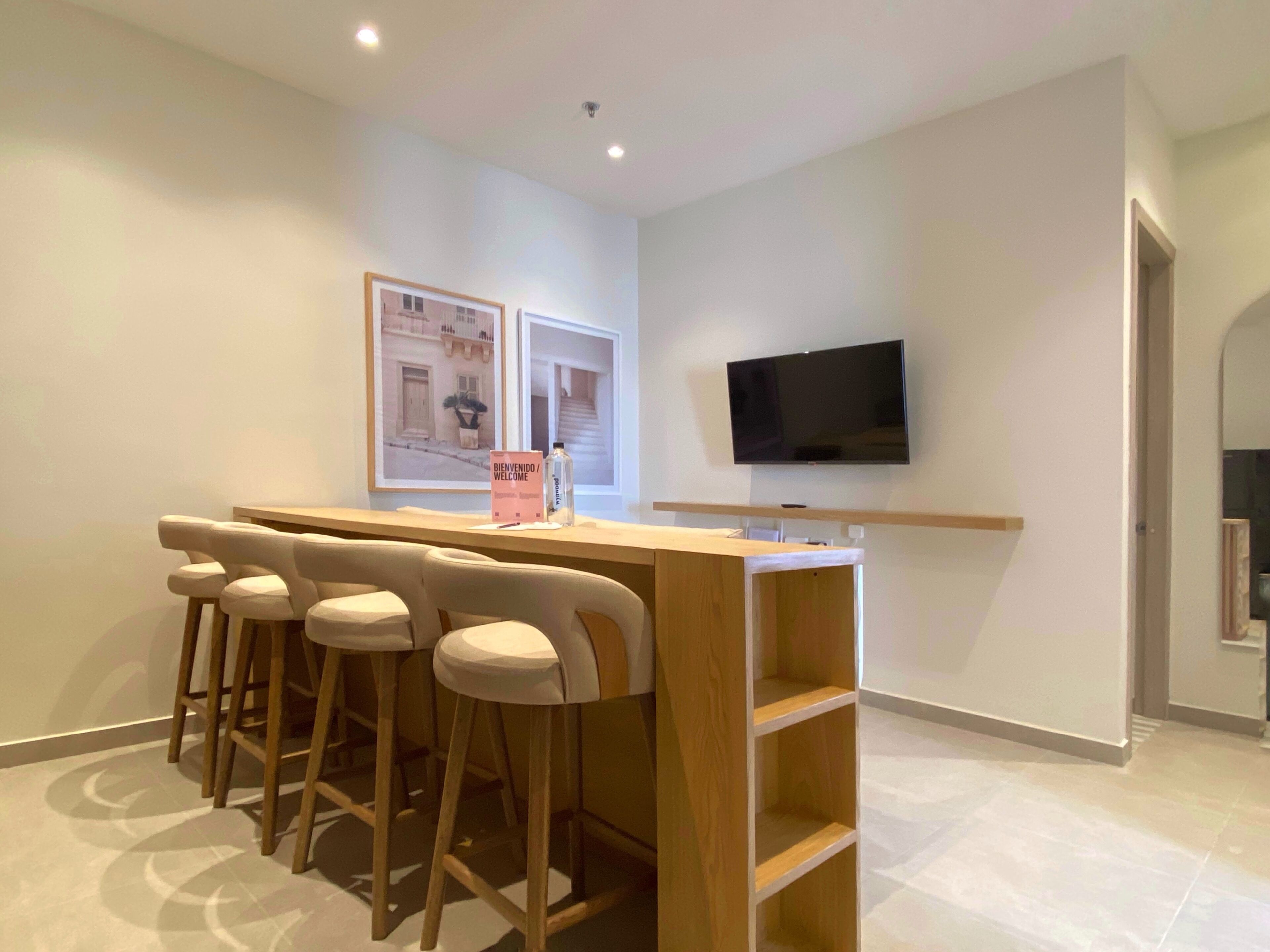 A modern kitchen with a bar area, wooden stools, a flat-screen TV, and framed pictures on the wall.