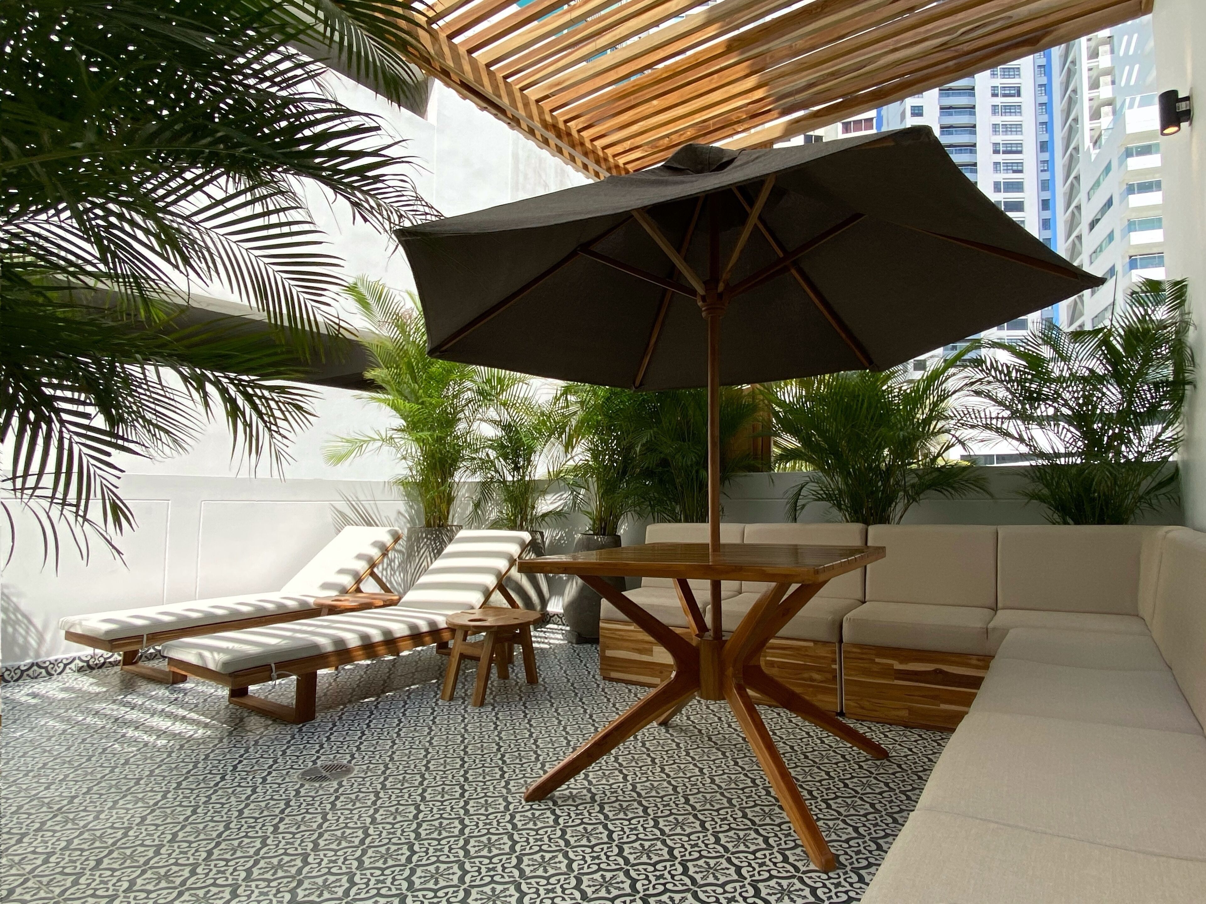 A modern outdoor lounge area with a wooden table, lounge chairs, and a sofa under a wooden pergola.
