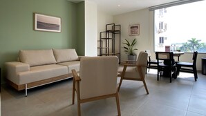Un soggiorno moderno con un divano color beige, sedie di legno, un tavolino e una pianta in vaso.