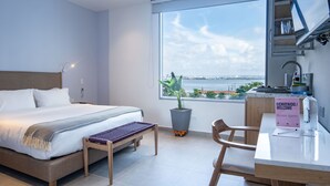 Una camera d'albergo moderna con un letto grande, una scrivania, una pianta in vaso e vista sul mare.