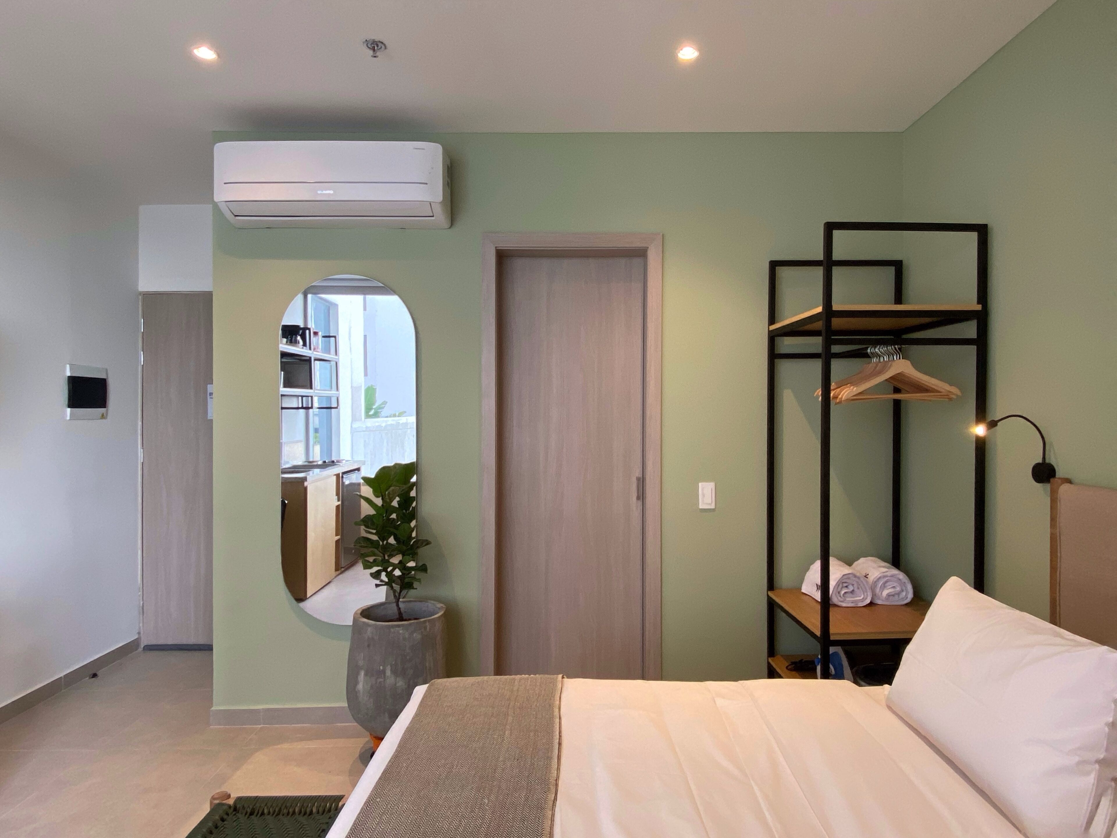 A modern bedroom with a bed, a mirror, a potted plant, a wardrobe, and a hanging shelf with towels.