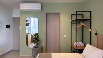 A modern bedroom with a bed, a mirror, a potted plant, a wardrobe, and a hanging shelf with towels.