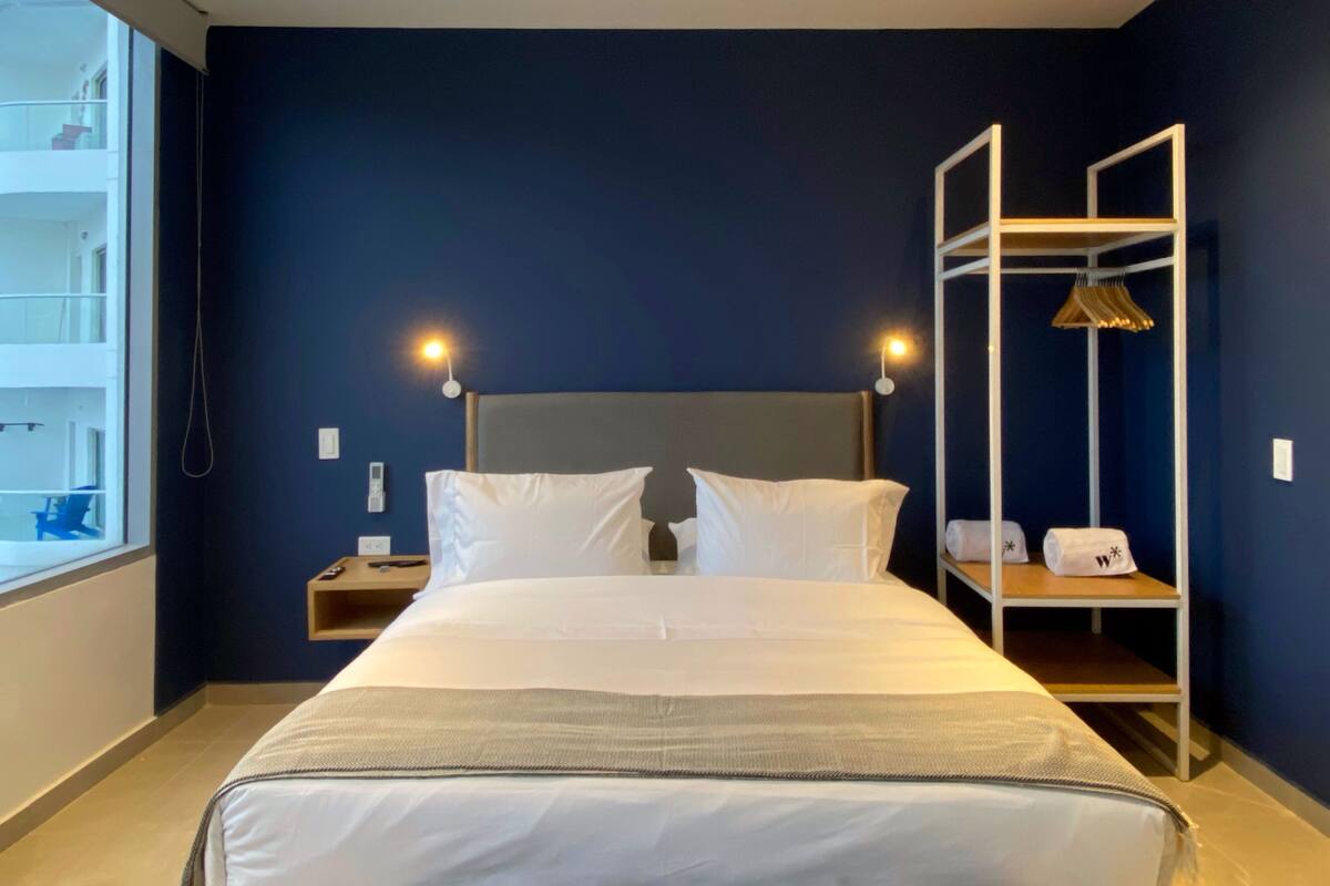 Ein Hotelzimmer mit einem großen Bett, zwei Nachttischlampen, einem Nachttisch, einem Kleiderschrank und Blick auf den Außenbalkon.
