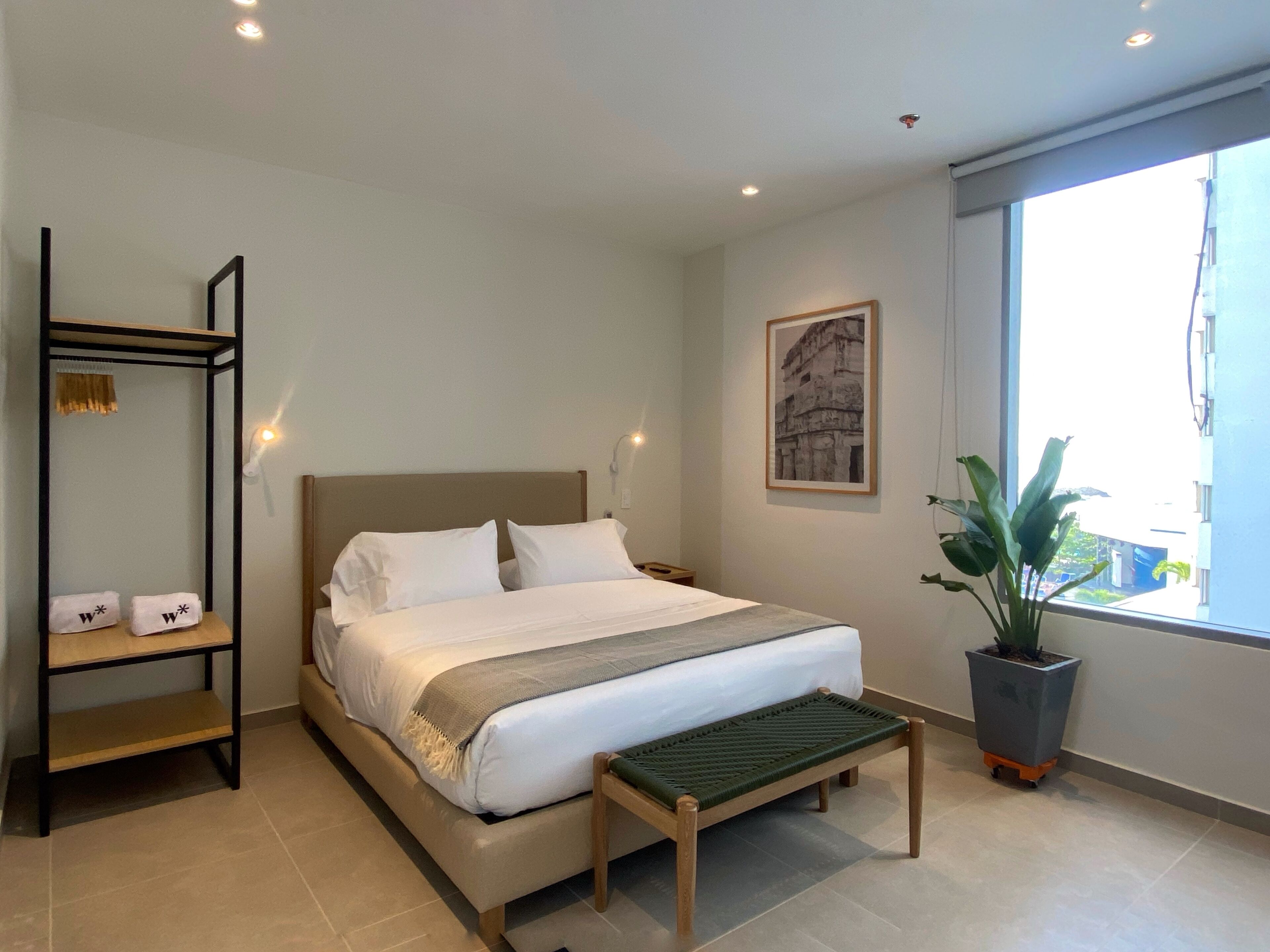 A modern bedroom with a bed, bedside tables, a bench, a potted plant, and a window with a view.