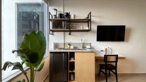 Una cucina moderna con lavastoviglie integrata, forno a microonde e macchina da caffè su uno scaffale. C'è una TV montata a parete e un'ampia finestra che offre luce naturale.