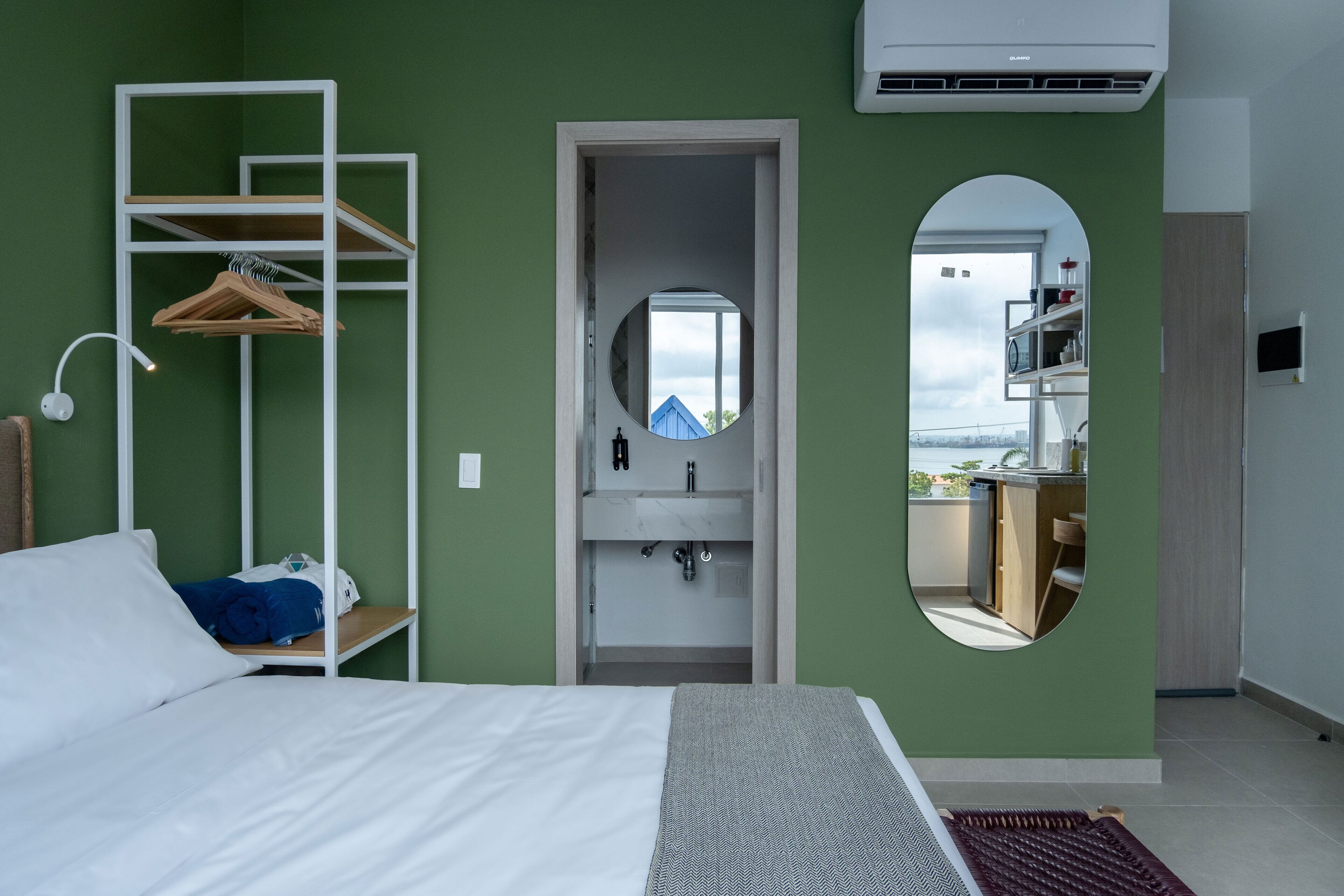 Ein Schlafzimmer mit einem Bett, einem an der Wand befestigten weißen Regal mit Kleidung, einem Spiegel und Blick auf einen Balkon.