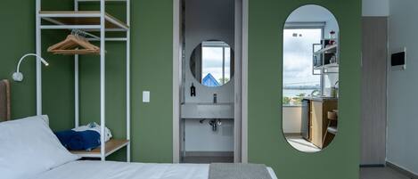 Ein Schlafzimmer mit einem Bett, einem an der Wand befestigten weißen Regal mit Kleidung, einem Spiegel und Blick auf einen Balkon.