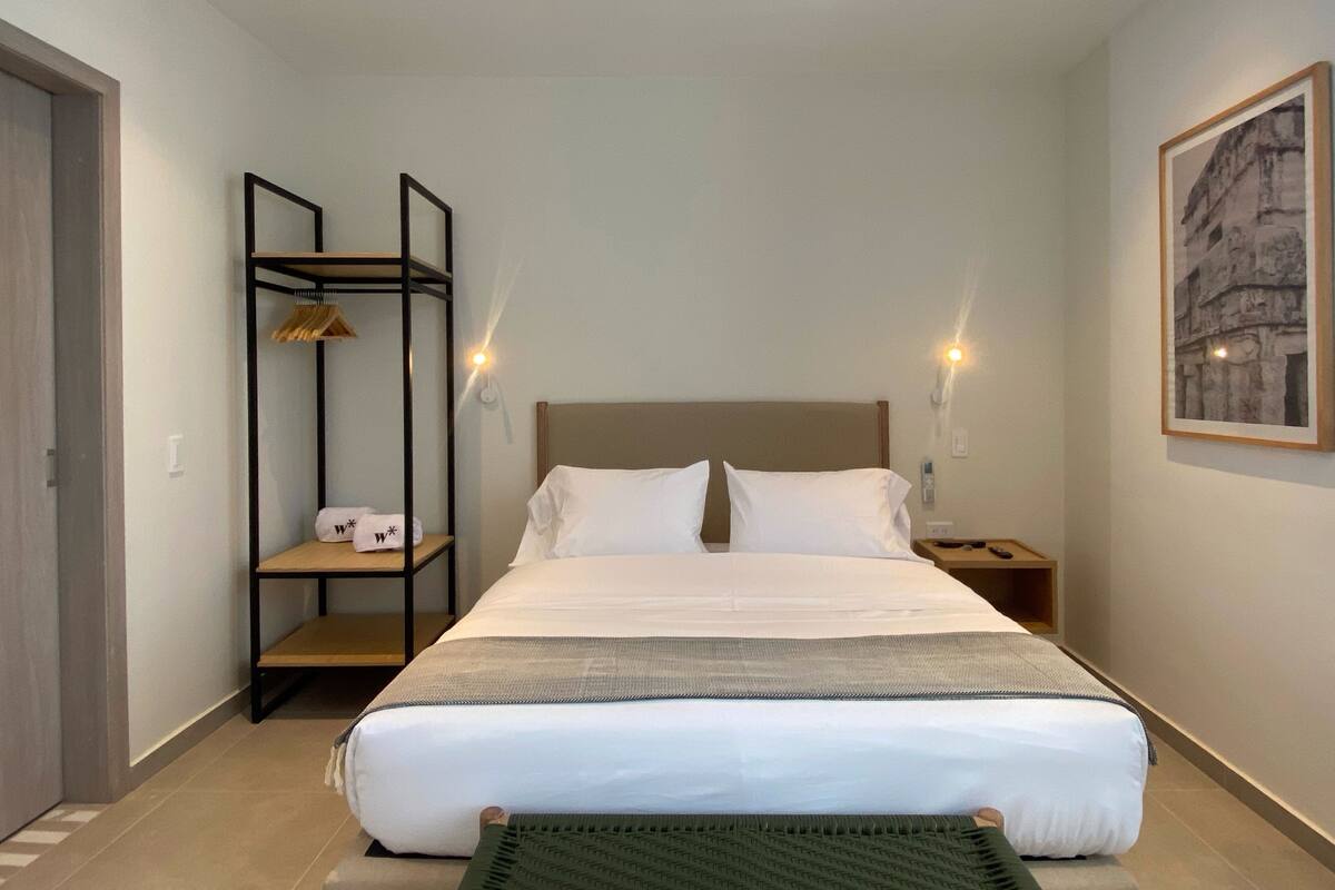 Ein ordentlich eingerichtetes Hotelzimmer mit einem großen Bett, einem Nachttisch, einer Wandablage und einem gerahmten Bild an der Wand.