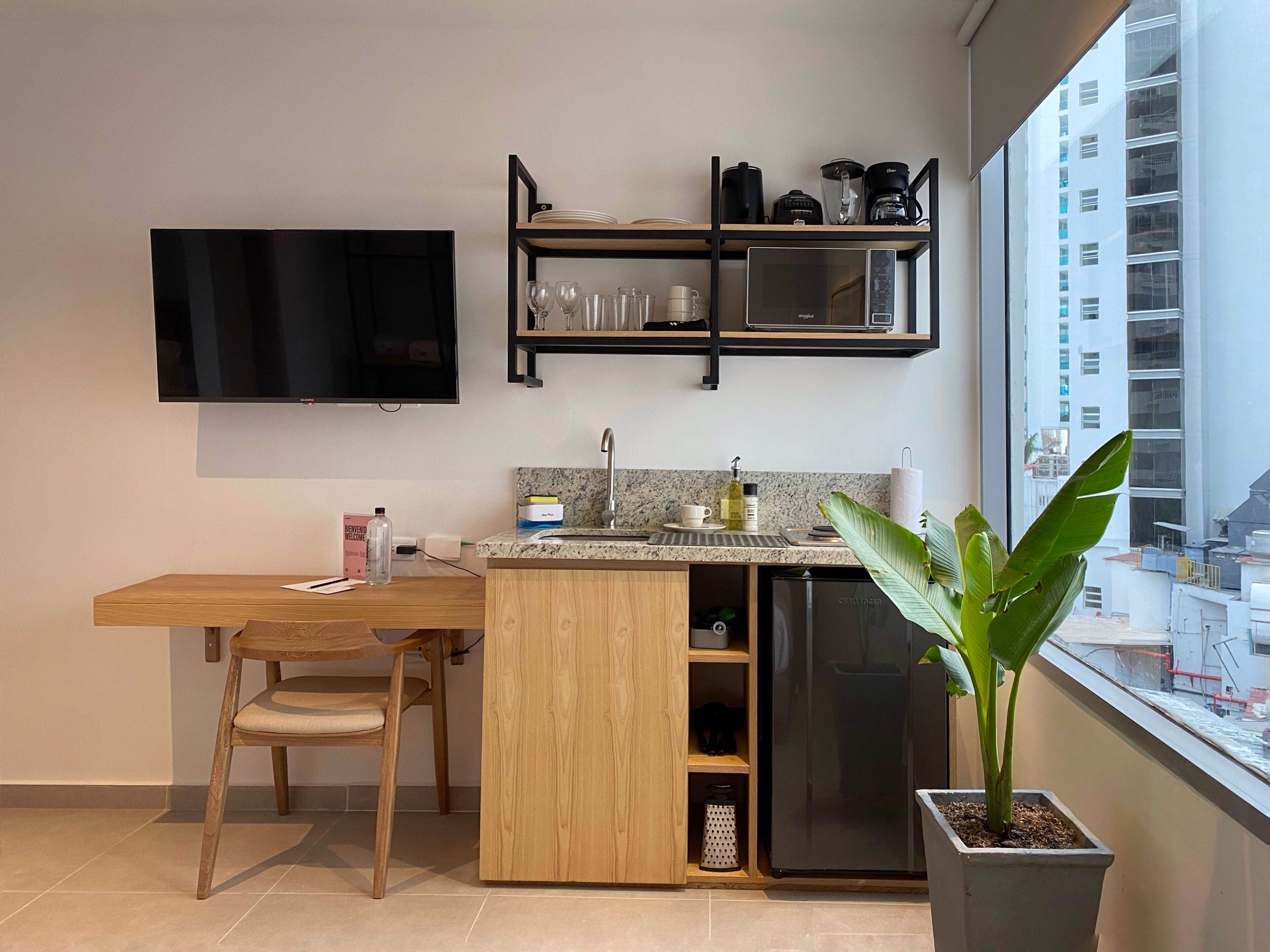 A modern kitchen with a wooden dining table, a built-in TV, and a potted plant.