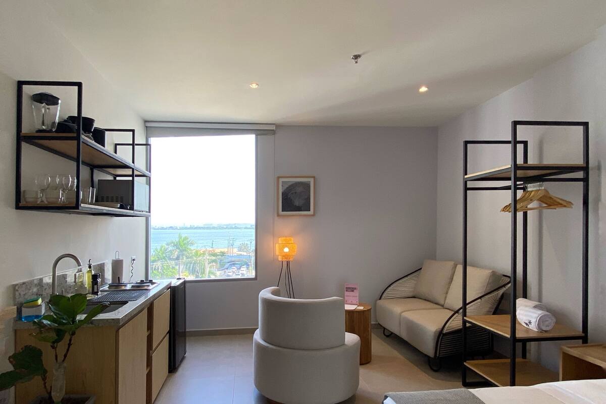 Ein modernes Hotelzimmer mit Küchenzeile, einer Sitzecke mit Sofa und Sessel sowie einem Bett und Meerblick.