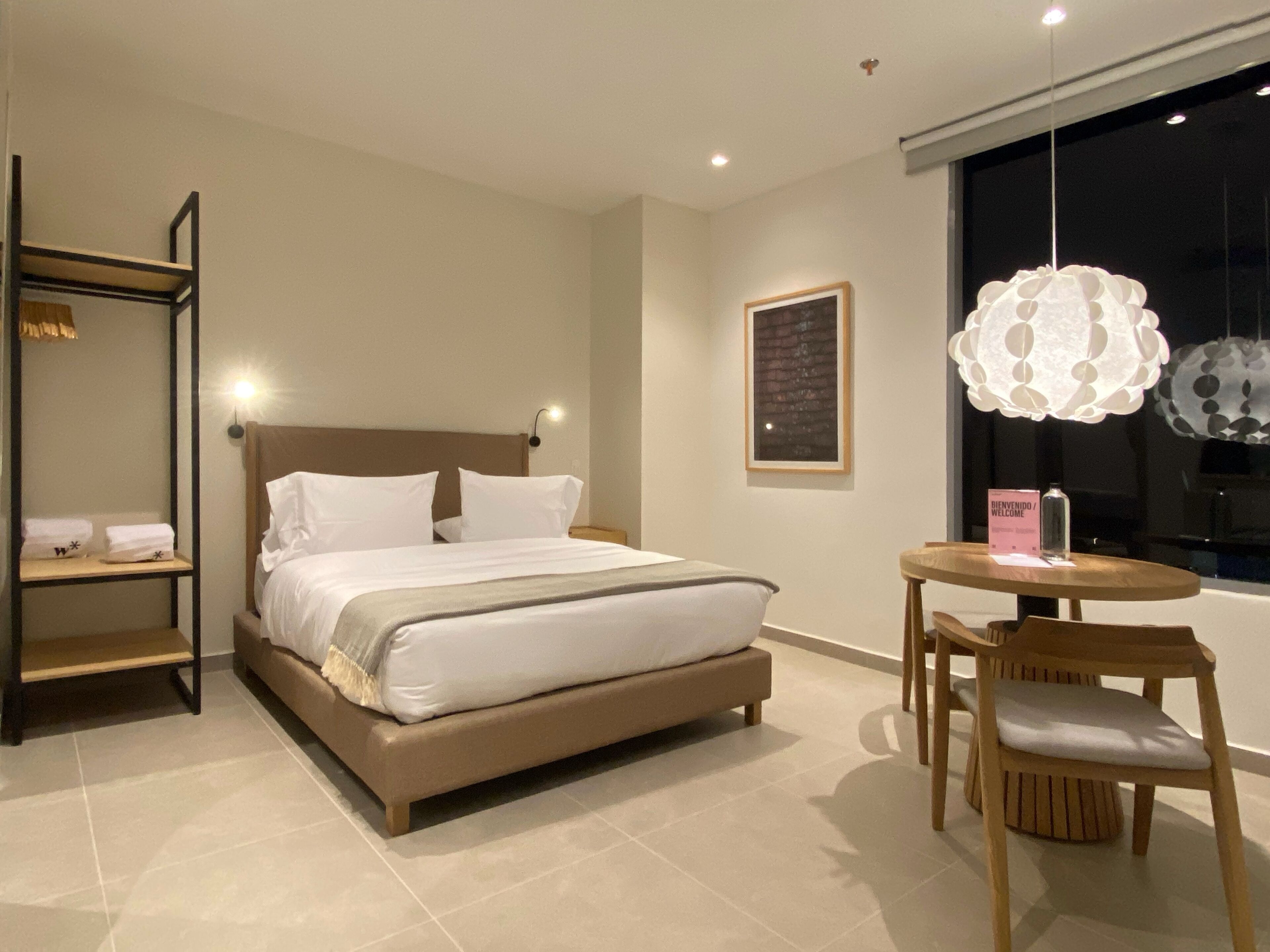 Une chambre d’hôtel moderne avec un grand lit, une table de chevet, une chaise et un lustre original.