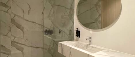 A modern bathroom with a marble vanity, a glass-enclosed shower, and a round mirror.