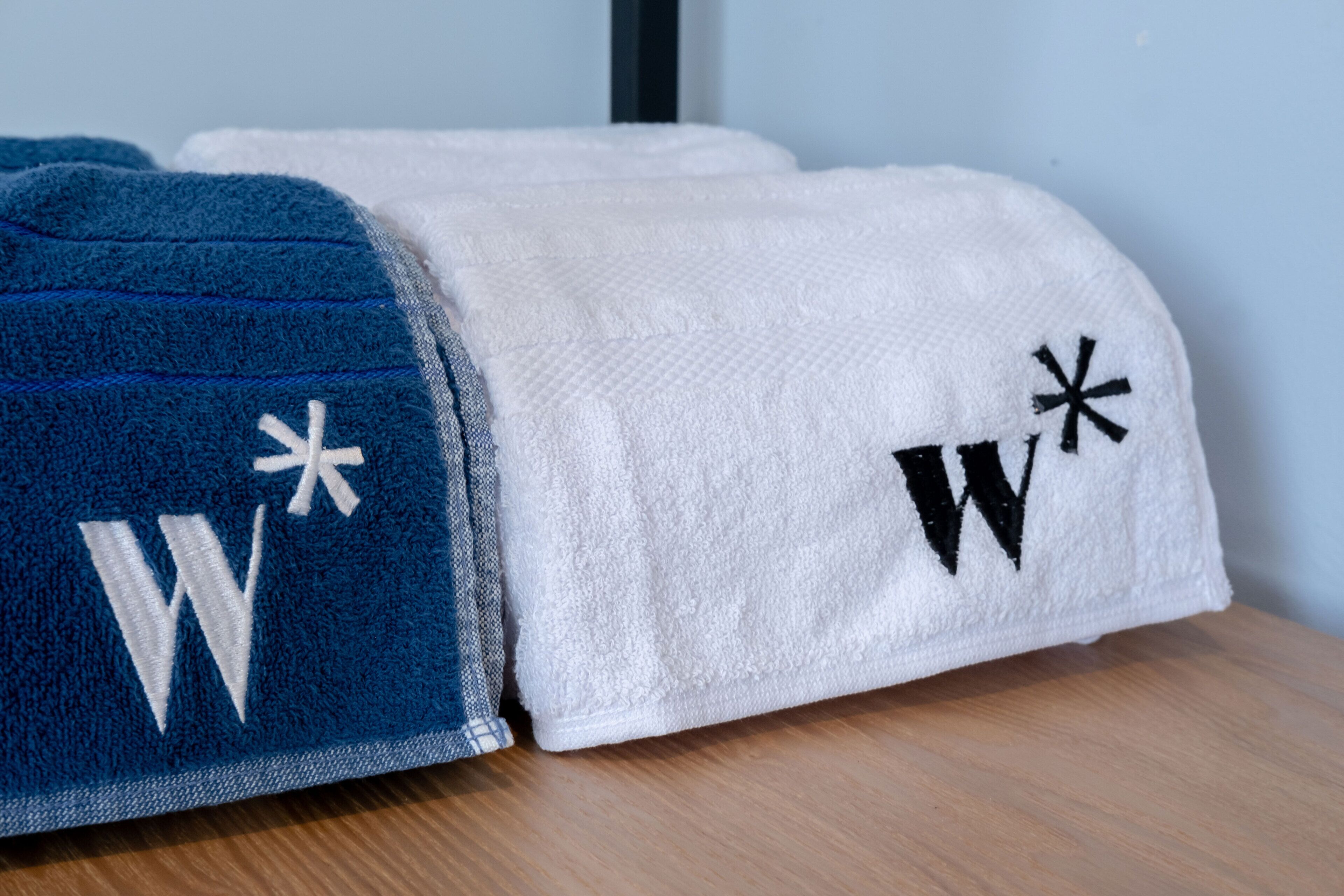Deux serviettes, une bleue et une blanche, ornées de lettres et d’astérisques brodés.