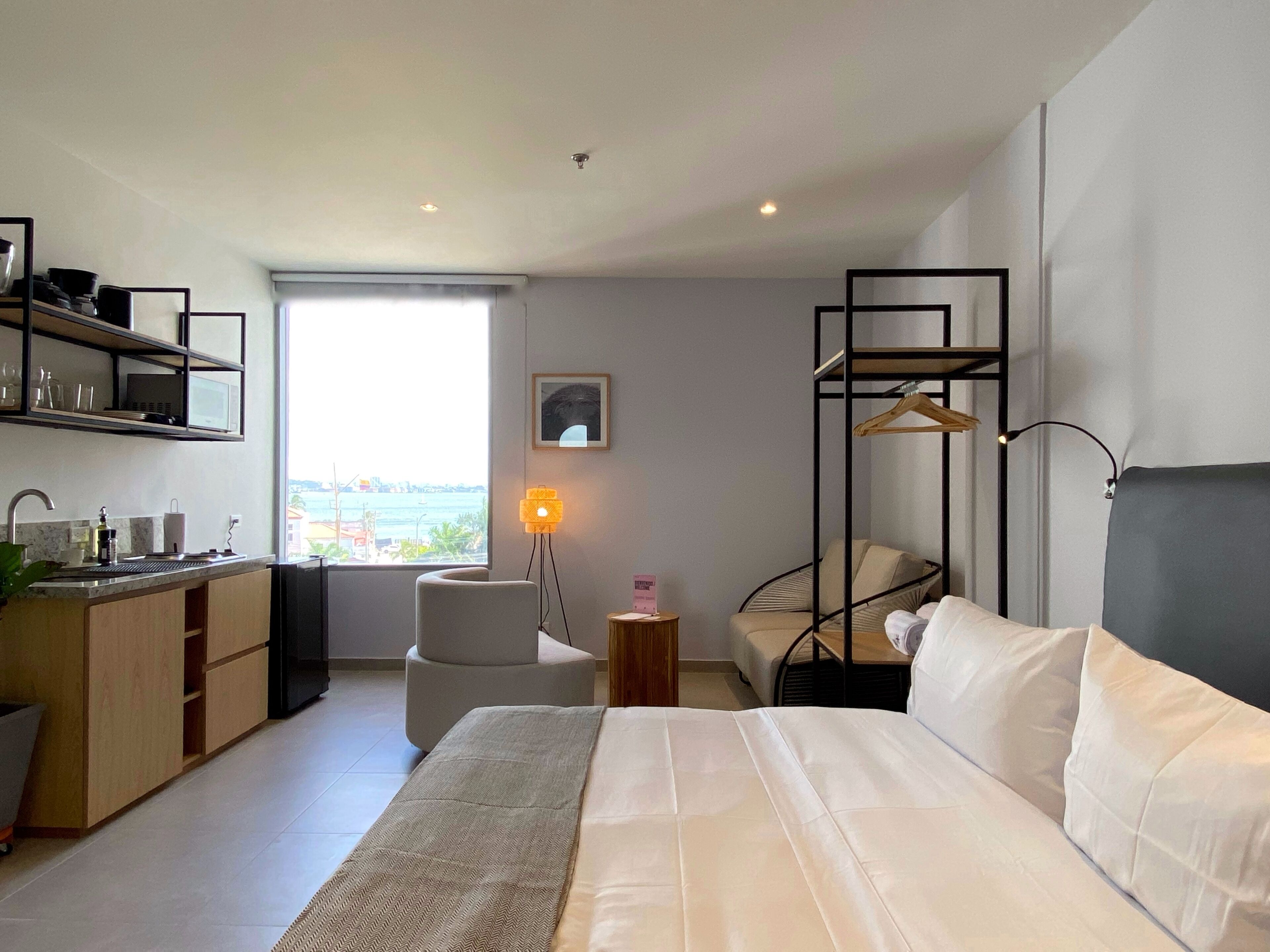 A modern hotel room with a bed, a desk, a chair, and a view of the sea.