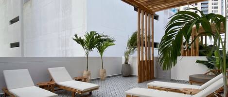 A rooftop lounge area with wooden loungers, potted plants, and patterned flooring.