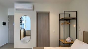 A modern hotel room with a bed, a wardrobe with a mirror, a small table with towels, and an air conditioning unit.