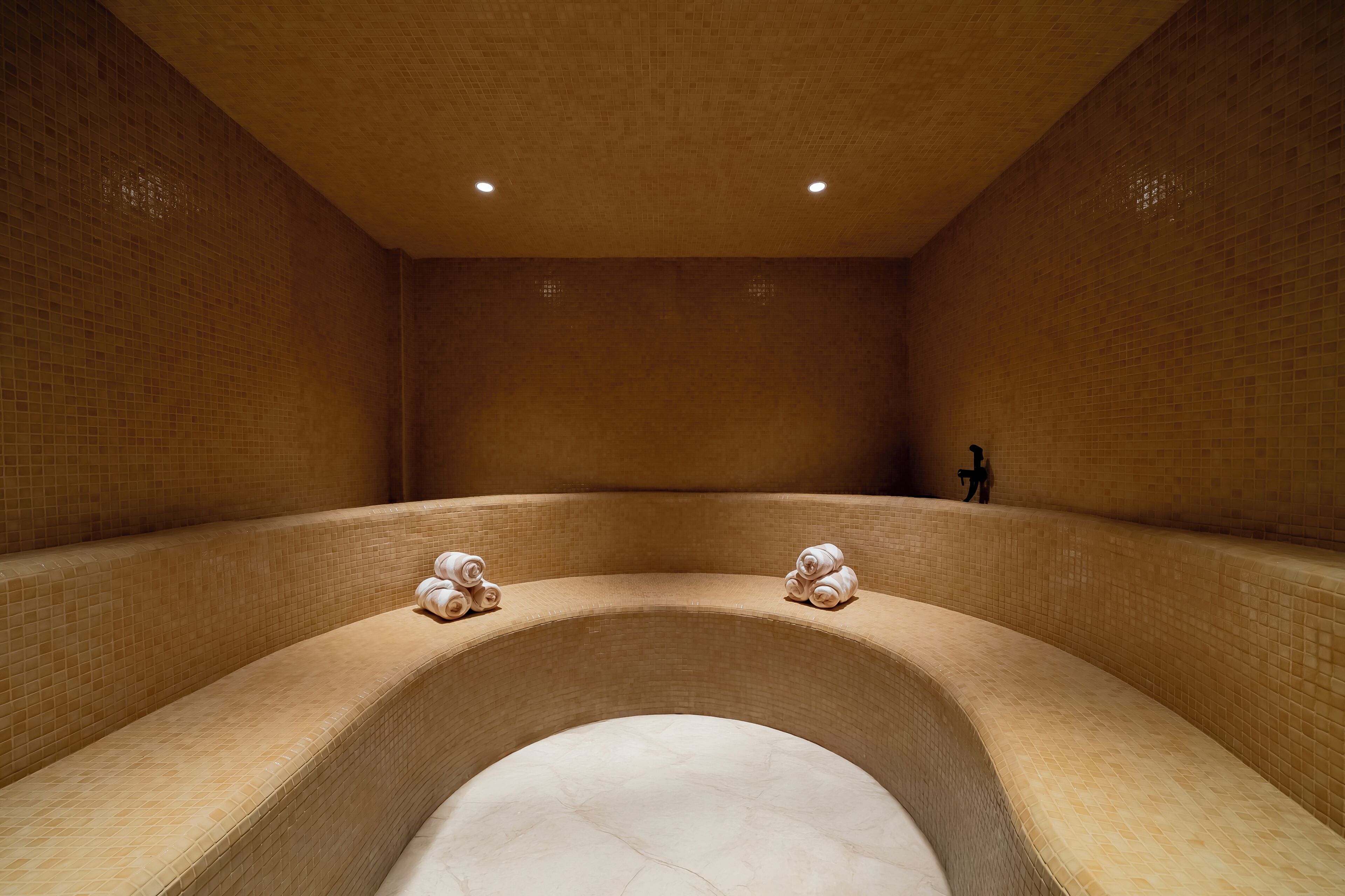A spa room with a curved bathtub, tiled walls, and two towels on the edge.