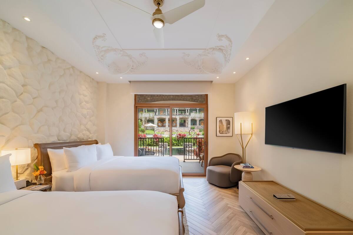 Une chambre d’hôtel avec deux lits, une télévision, un bureau et un balcon donnant sur une cour.