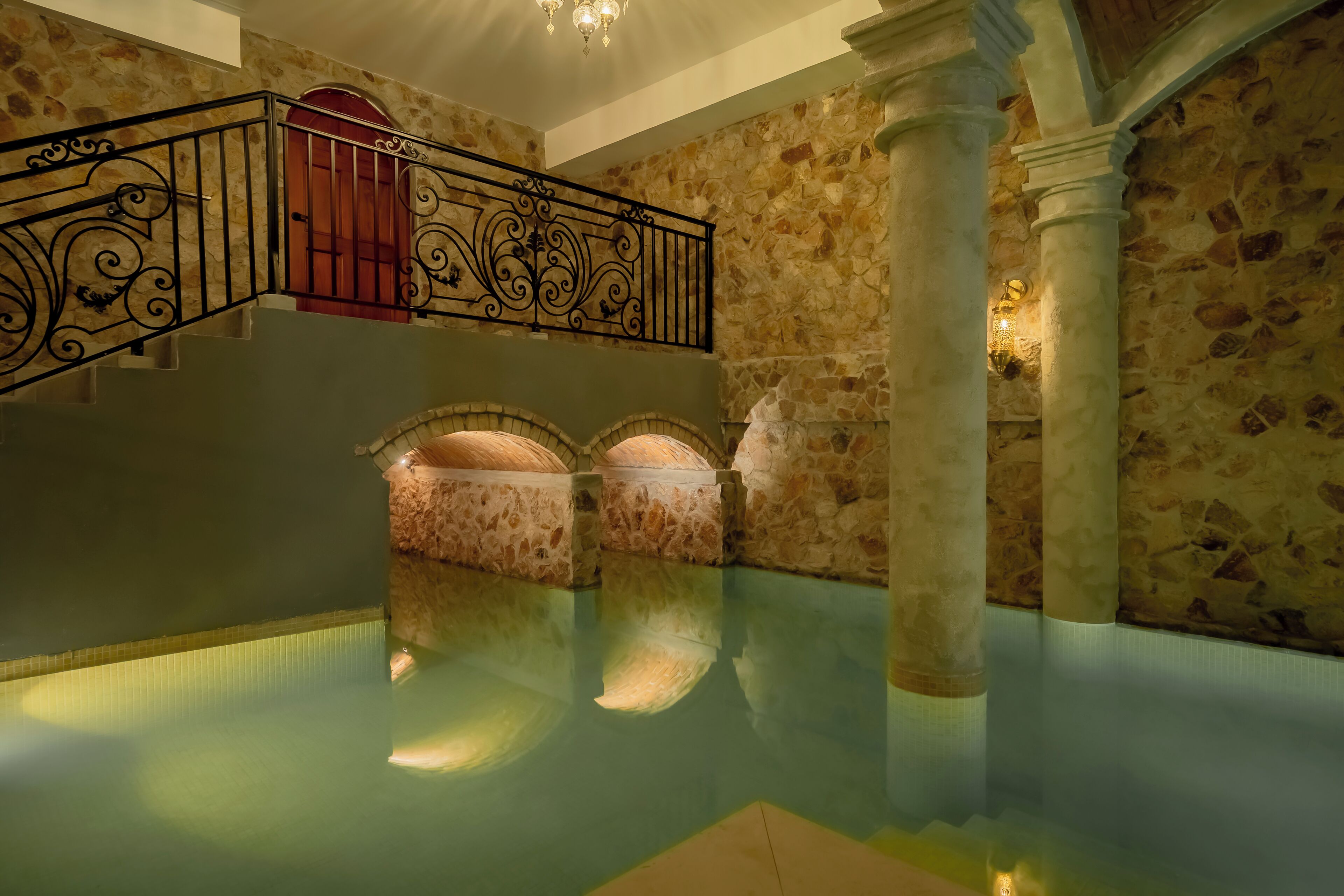 Zona de piscina interior con paredes de piedra, barandilla de metal y una escalera que lleva a un nivel superior.