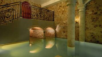 Zona de piscina interior con paredes de piedra, barandilla de metal y una escalera que lleva a un nivel superior.