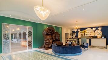 A hotel lobby with a reception desk, a large sculpture, and a bar area.