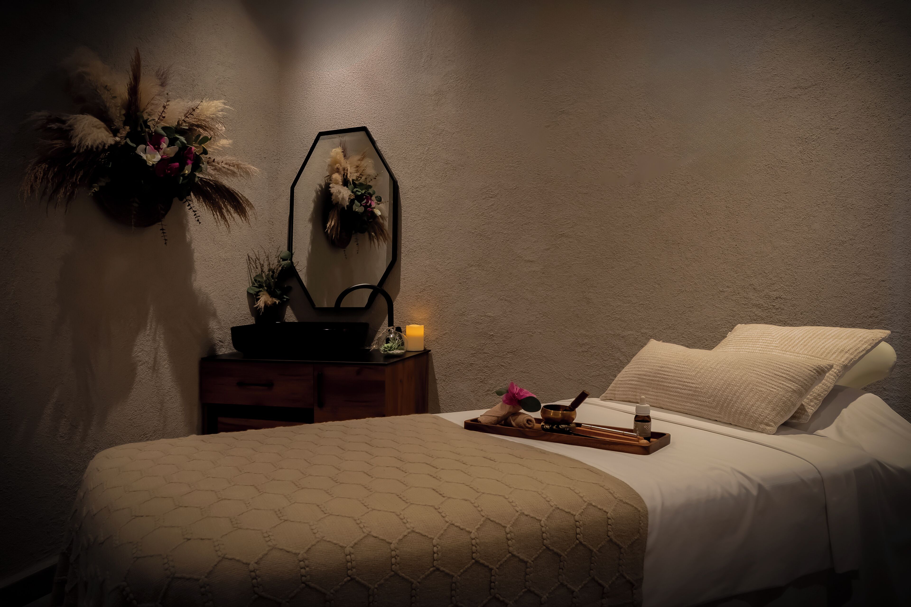 A neatly made bed with a patterned bedspread, a bedside table with a candle, a mirror, and a decorative wall hanging.