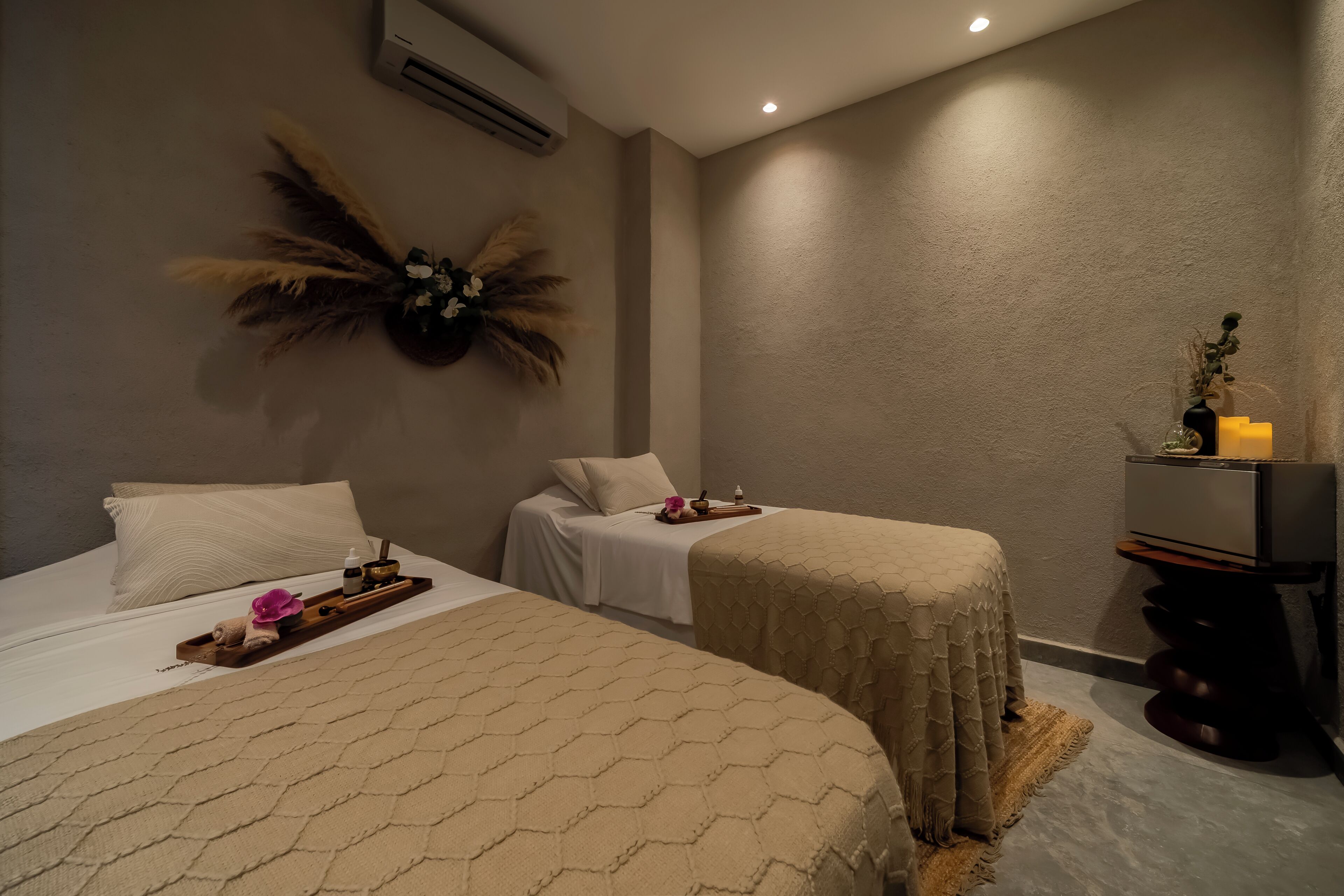 A hotel room with two beds, a small table with toiletries, a decorative wall piece, and a TV stand.