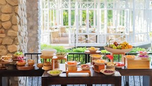 A breakfast buffet with various food items and a view of a garden through a glass enclosure.