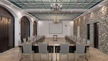 Un salón de conferencias con una larga mesa, sillas, una pantalla de proyector y una pared de piedra.