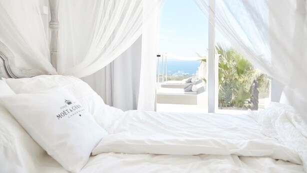 A bed with white bedding and a pillow with text, a canopy, and a view of the sea through large windows. - Beautiful Villa With sea Views (Sant Josep de sa Talaia)