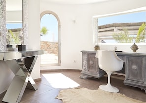 A modern interior with a glass desk, a white chair, and a stone wall. - Beautiful Villa With sea Views (Sant Josep de sa Talaia)