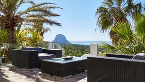 An outdoor patio with wicker furniture and a view of a mountain and ocean. - Beautiful Villa With sea Views (Sant Josep de sa Talaia)