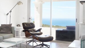 A modern living room with a leather chair, a glass table, and a view of the sea through large sliding doors. - Beautiful Villa With sea Views (Sant Josep de sa Talaia)