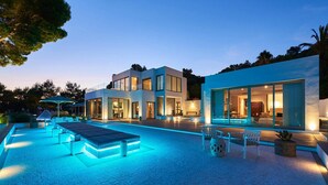 Ein modernes Haus mit Swimmingpool, Sitzgelegenheiten im Freien und großen Fenstern.