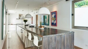 A modern kitchen with a central island, bar stools, pendant lighting, and a large window. - Super Villa With Swimming Pool (Sant Josep de sa Talaia)