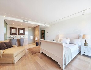 A modern hotel room with a large bed, a sofa, a bathroom with a shower, and a small desk. - Super Villa With Swimming Pool (Sant Josep de sa Talaia)